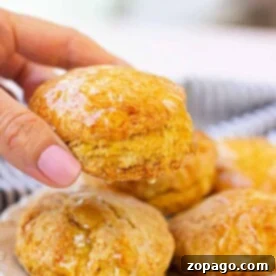 Sweet Honey Biscuits 6 A hand holding a glazed honey biscuit delicately over a plate of assorted biscuits.