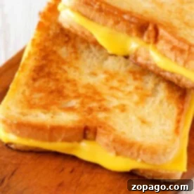 Two golden brown grilled cheese sandwiches, perfectly crisp from the toaster oven, are stacked on a wooden board.