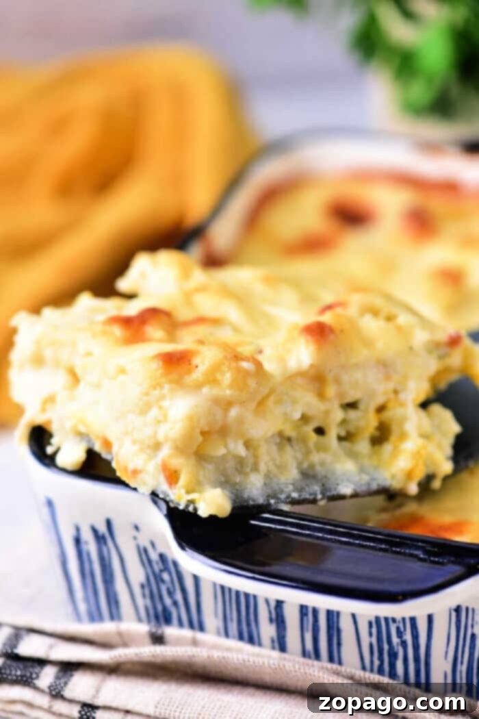 Ultimate Cheesy Cauliflower Gratin 2 A slice of creamy baked mac and cheese cauliflower, reminiscent of a cheesy cauliflower bake, on a spatula above a blue casserole dish.