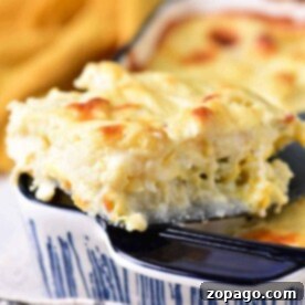 Close-up of a slice of creamy cheesy cauliflower bake, being served from a blue ceramic dish.