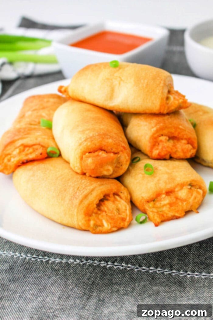 Crispy Buffalo Chicken Rolls 2 Buffalo Chicken Crescent Rolls piled high on a plate, garnished with green onions and a side of dipping sauce.