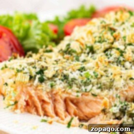 Fragrant Herb Crusted Salmon 6 Close-up of herb-crusted salmon fillet with a crispy finish on a white plate, garnished with lettuce and tomato slices.