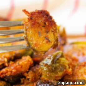 Close-up of a fork holding a crispy, Parmesan-crusted Brussels sprout slice with more on a white and blue-rimmed plate.
