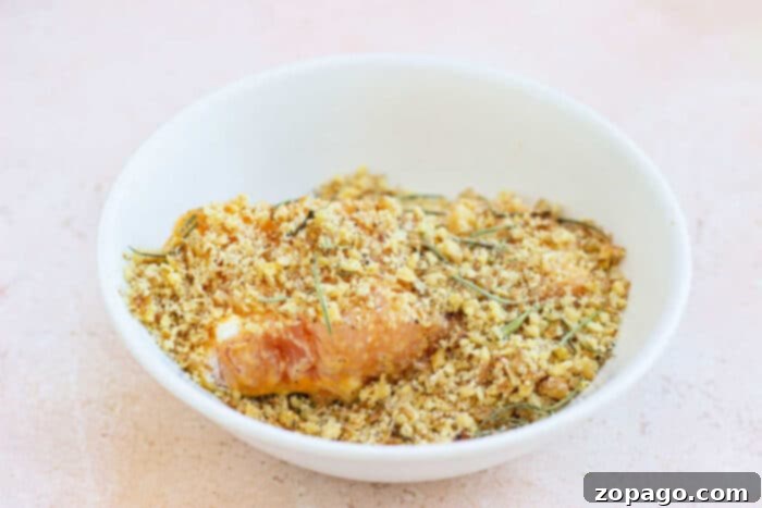 Golden Pecan Crusted Oven Trout 4 A white bowl filled with seasoned breadcrumbs and a fish fillet sits on a light surface, hinting at the nutty flavor of a pecan-crusted trout experience.