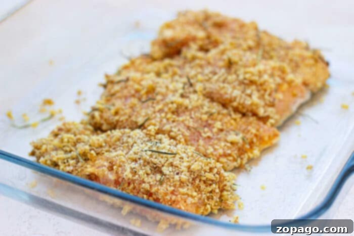 Golden Pecan Crusted Oven Trout 5 Breaded fish fillets with herbs, reminiscent of pecan-crusted trout, sit in a glass baking dish, ready for cooking.