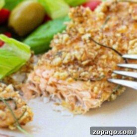 Pecan crusted trout filet with a fork, accompanied by a fresh salad of lettuce, tomatoes, and olives on a white plate.