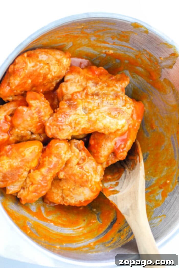 Tangy Buffalo Chicken Thighs 6 Buffalo chicken thighs with spicy sauce in a metal bowl, with a wooden spoon nestled beside them.