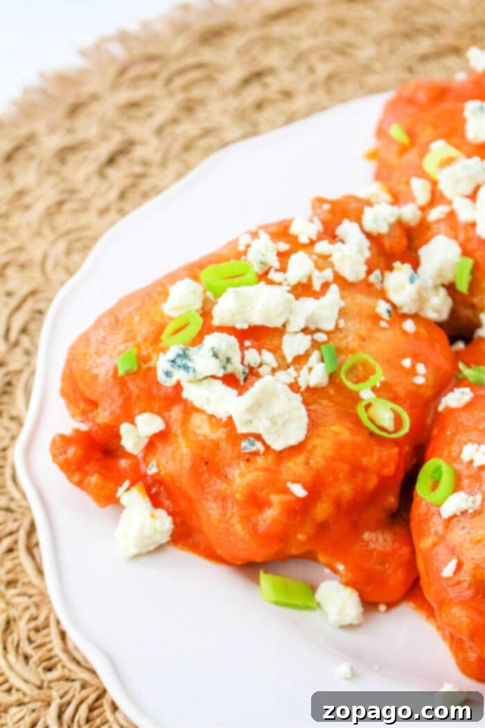 Tangy Buffalo Chicken Thighs 7 Buffalo chicken thighs are topped with blue cheese crumbles and sliced green onions, elegantly displayed on a white plate.