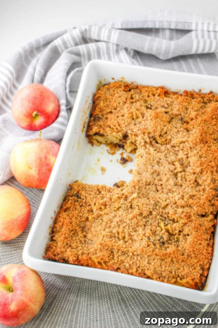 Apple Bake 6 A delightful apple kugel sits invitingly in a white baking dish, reminiscent of a comforting apple kugel, with three fresh apples and a charming striped cloth nearby.