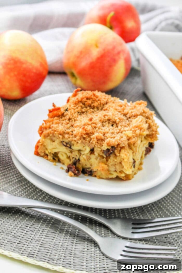 Apple Bake 8 A slice of apple kugel cake, reminiscent of a classic apple kugel, sits on a white plate surrounded by whole apples and forks.