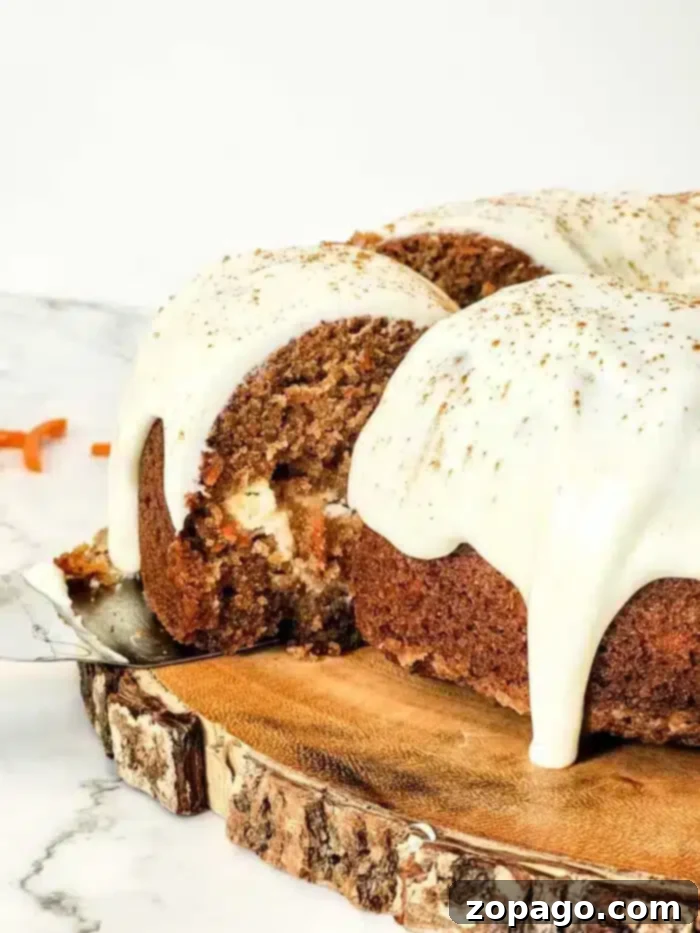 Spiced Carrot Bundt Cake 2 A slice of sumptuous carrot Bundt cake with cream cheese frosting is being served. The cake rests elegantly on a wooden platter. The thick frosting drapes the top, with grated carrots adding a rustic touch nearby on the marble surface.