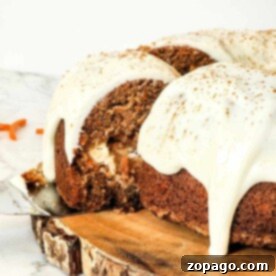 Carrot Bundt cake with cream cheese frosting rests elegantly on a wooden platter, one enticing slice being lifted out.