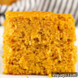 A close-up of a square piece of sweet potato cornbread on a white surface, showcasing its soft, crumbly texture.