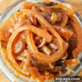 A jar filled with rich, slow cooker caramelized onions rests invitingly on a rustic wooden board.
