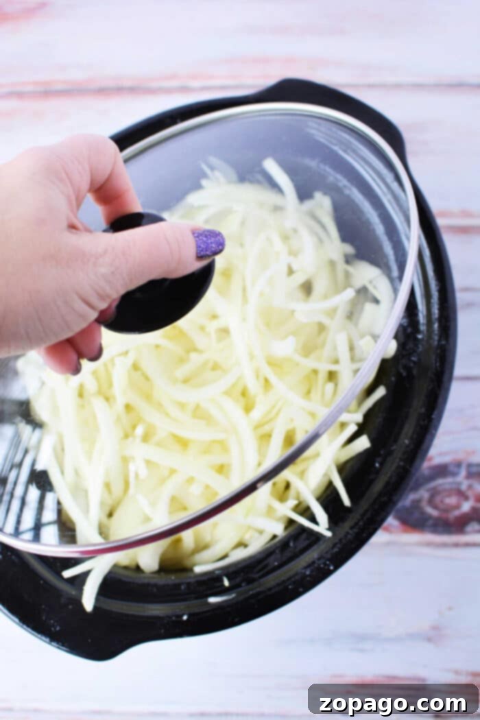Slow Cooker Onion Gold 7 Hand lifting lid from slow cooker filled with shredded potatoes and caramelized onions, ready to be served.