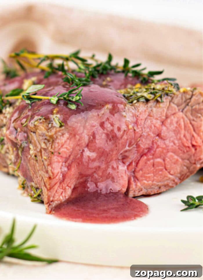 Savory Bottom Round Roast 2 Juicy, medium-rare bottom round roast beef steak topped with herbs and red sauce on a white plate, ready to be served