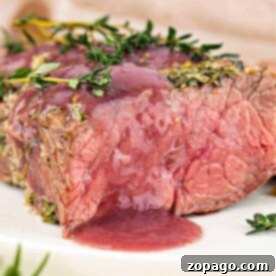 Savory Bottom Round Roast 10 A juicy, medium-rare bottom round roast beef steak topped with herbs and red sauce on a white plate.