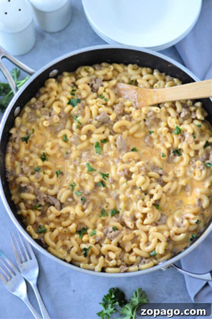 Creamy Cheesy Beef and Pasta Skillet 5 Homemade Hamburger Helper with Velveeta: A close-up of a wooden spoon stirring the creamy, cheesy macaroni and ground beef in a skillet.