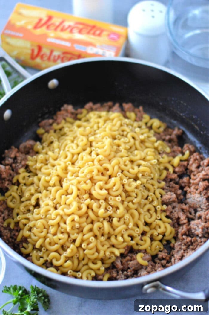 Creamy Cheesy Beef and Pasta Skillet 7 Homemade Cheeseburger Helper Recipe: A close-up of the finished dish in a skillet, garnished with fresh green herbs, ready to be served.