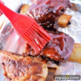 Coating beef ribs in a rich sauce with a red brush on a foil-lined tray, preparing them for slow roasting in the oven at 275.