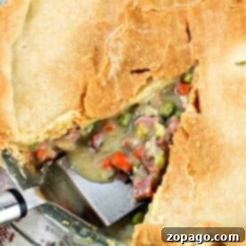 A golden-crusted Ham Pot Pie, with a slice removed to reveal a filling of ham, peas, carrots, and creamy sauce.