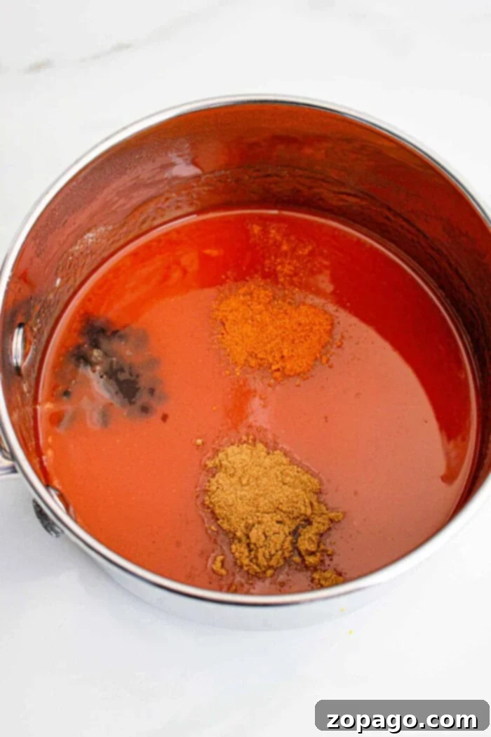 Popeyes Tangy Sweet Heat 6 A steel pot brimming with a medley of spices evokes the vibrant kick of Popeyes Sweet Heat Sauce, all resting on a pristine white surface.