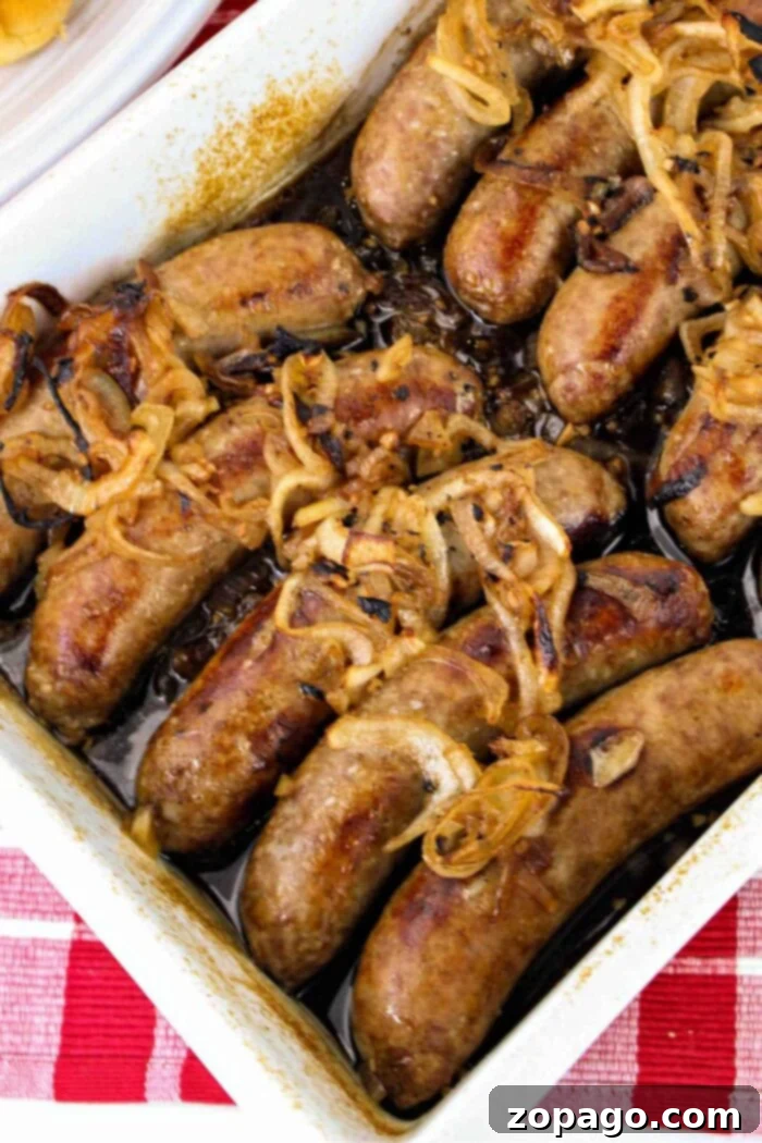 Perfectly Cooked Bratwurst Every Time 2 A rectangular baking dish filled with cooked sausages topped with caramelized onions sits enticingly on a red and white checkered tablecloth, making you wonder how to cook bratwurst to perfection.