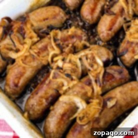 A rectangular baking dish filled with cooked sausages topped with caramelized onions sits enticingly on a red and white checkered tablecloth, making you wonder how to cook bratwurst to perfection.