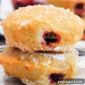 Irresistible Air Fryer Jelly Donuts 7 Two air fryer jelly-filled doughnuts stacked on a glass plate.