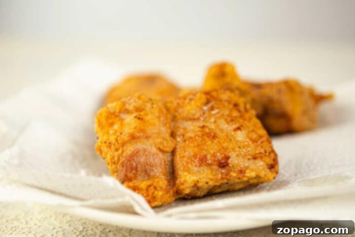 Golden Crispy Pork Chops 6 Close-up of crispy fried pork pieces, reminiscent of deep-fried pork chops, resting on a paper towel-lined plate.