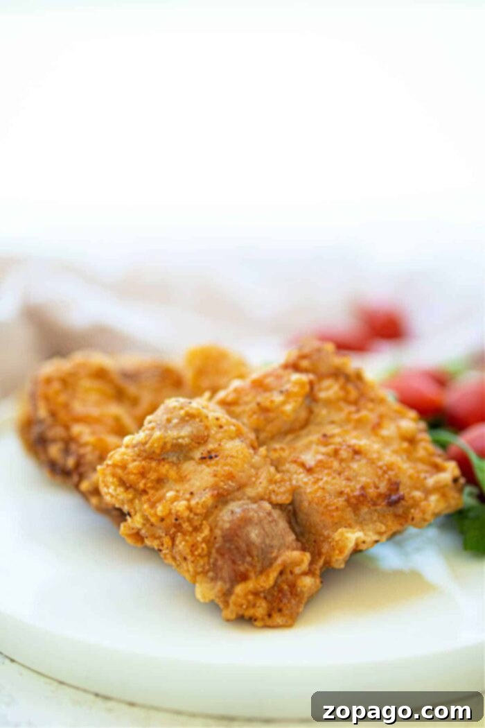 Golden Crispy Pork Chops 7 Crispy fried pork pieces share the plate with deep-fried pork chops, while cherry tomatoes brighten the background.