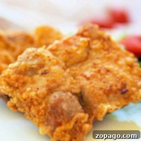 Close-up of a crispy deep fried pork chops and blurred vegetables in the background.