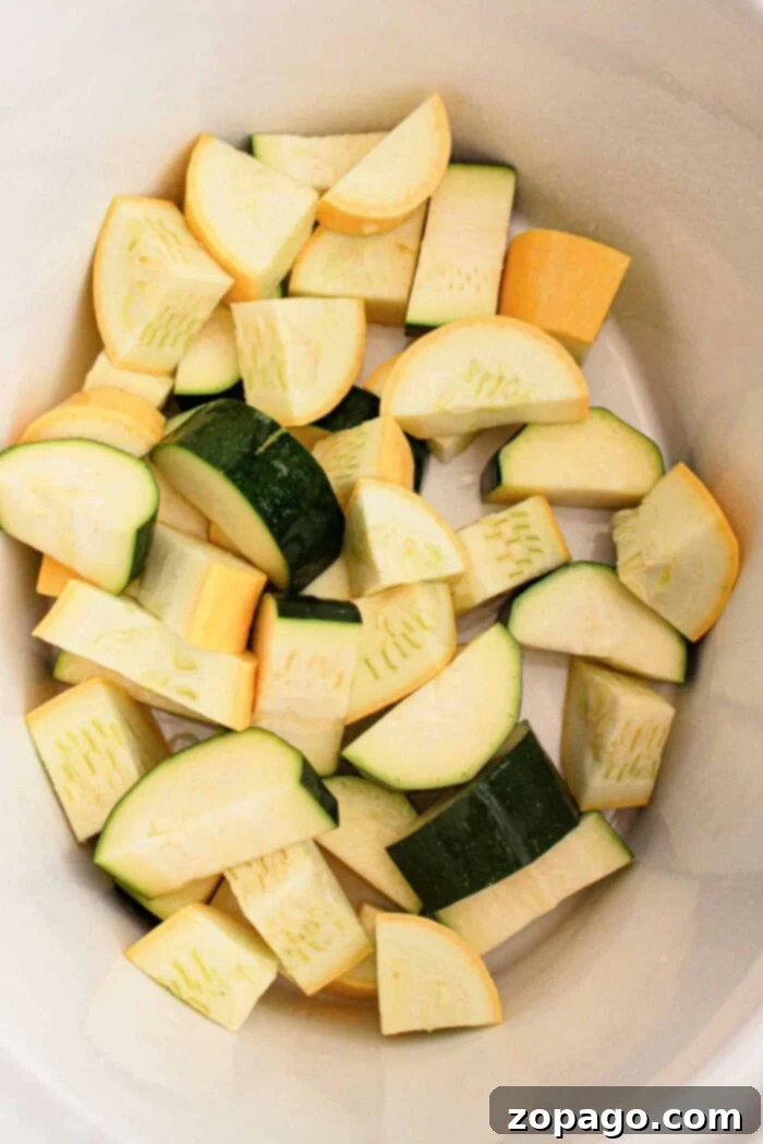 Effortless Slow Cooker Vegetables 4 The image shows chopped pieces of zucchini and yellow squash inside a white container. The vegetables, perfect for a slow cooker recipe, are cut into uniform chunks, displaying their green and yellow peels.