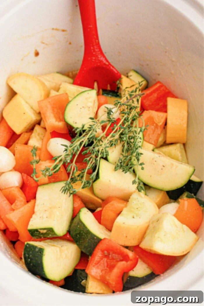 Effortless Slow Cooker Vegetables 6 A red spoon rests in a pot filled with chopped fresh vegetables, including zucchini, bell peppers, and onions. A sprig of thyme is placed on top, adding a touch of green to the mix. The seasoned vegetables appear ready for cooking in a slow cooker.