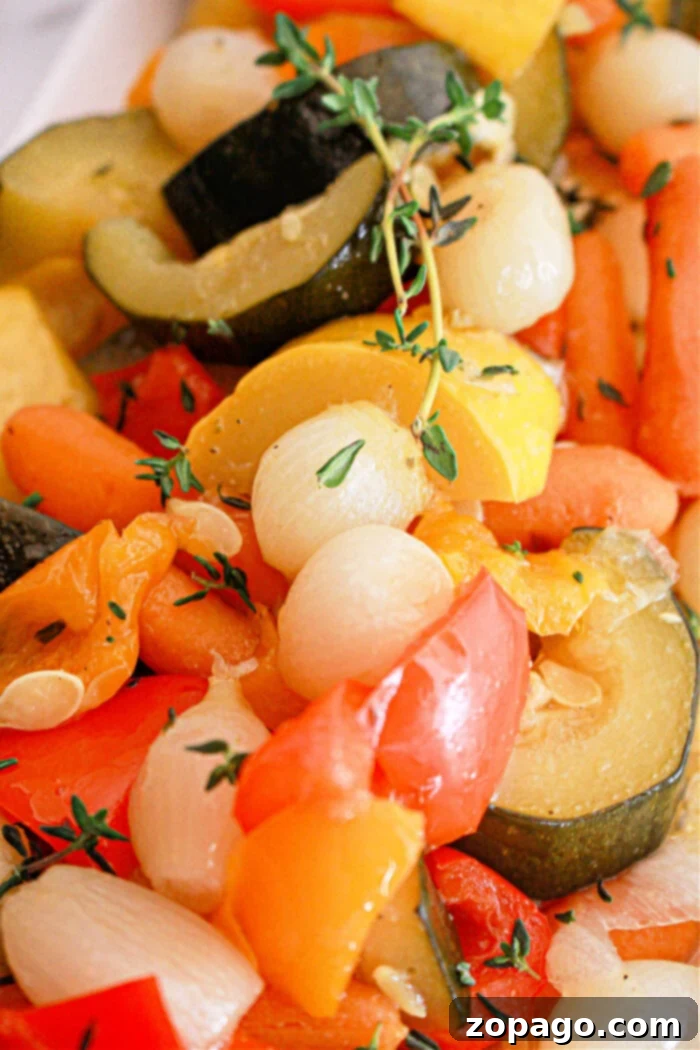Effortless Slow Cooker Vegetables 7 A close-up of a mixed vegetable medley featuring zucchini slices, baby carrots, pearl onions, and bell pepper pieces, garnished with sprigs of thyme. The Slow Cooker Vegetables appear to be cooked and seasoned, displaying vibrant colors.