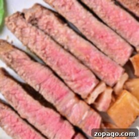 Cooking Beef Strip Loin Steaks to Perfection 6 A plate with several slices of medium-rare beef strip loin steaks arranged in a line. The meat is pink in the center with a browned outer edge, featuring a juicy texture. Some greens are visible in the corner of the plate, showing you how to cook beef strip loin steaks to perfection.