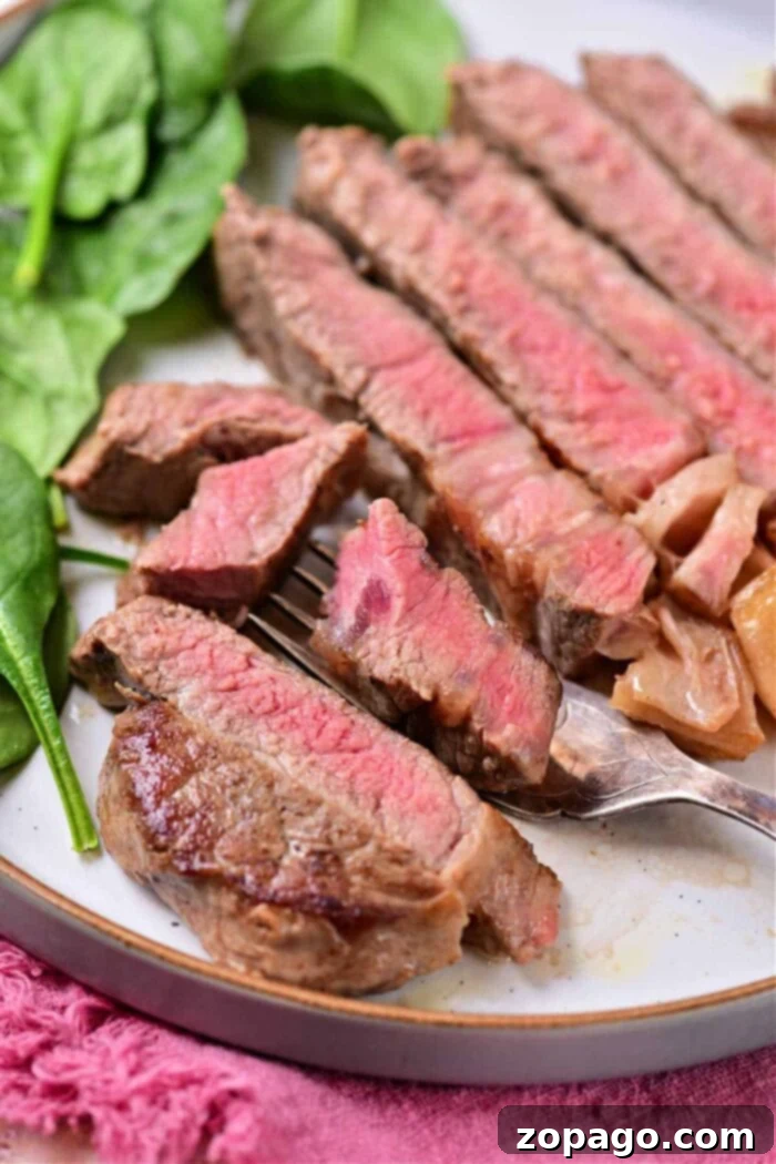 Cooking Beef Strip Loin Steaks to Perfection 7 A perfectly prepared plate features sliced medium-rare steak, exhibiting a vibrant pink center, characteristic of expertly cooked beef strip loin steaks. The tender slices are elegantly arranged next to a fresh leafy green, possibly spinach, offering a refreshing contrast. A fork delicately holds a piece of steak, inviting a taste, with a soft pink fabric subtly visible in the background, completing the refined presentation.