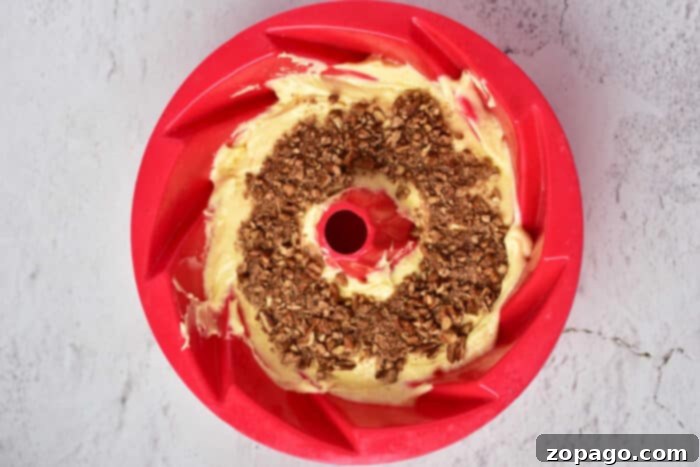Ultimate Sock It To Me Cake with Cake Mix 4 A bundt pan, half-filled with golden cake batter, revealing a delicious layer of cinnamon-pecan crumble at its center, ready for the final batter layer and baking.