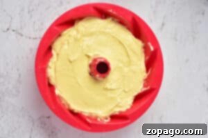 Ultimate Sock It To Me Cake with Cake Mix 9 A red bundt pan filled with yellow cake batter sits invitingly on a light gray surface, ready to transform into a delightful Sock it to me cake using a convenient cake mix.