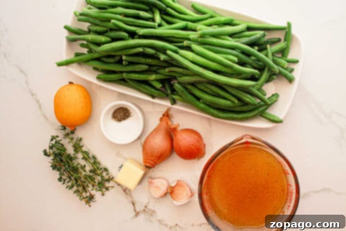 Effortless Crockpot Green Beans 4 A display of ingredients on a white marble surface: a rectangular dish filled with fresh green beans, perfect for the crockpot, a whole lemon, small glass bowls with black pepper and broth, two shallots, a pat of butter, two garlic cloves, and a few sprigs of thyme.