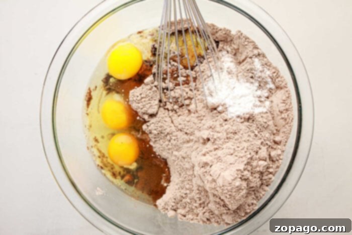 Effortless Brownie Cupcakes 4 A mixing bowl filled with eggs, flour, cocoa, and baking powder is being whisked together to create a rich brownie mix.