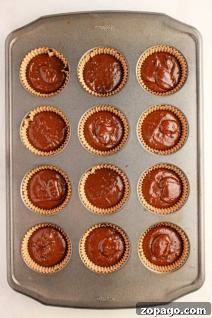 Effortless Brownie Cupcakes 5 A muffin pan holds twelve chocolate cupcake liners brimming with rich brownie mix, ready to transform into delectable brownie cupcakes in the oven.