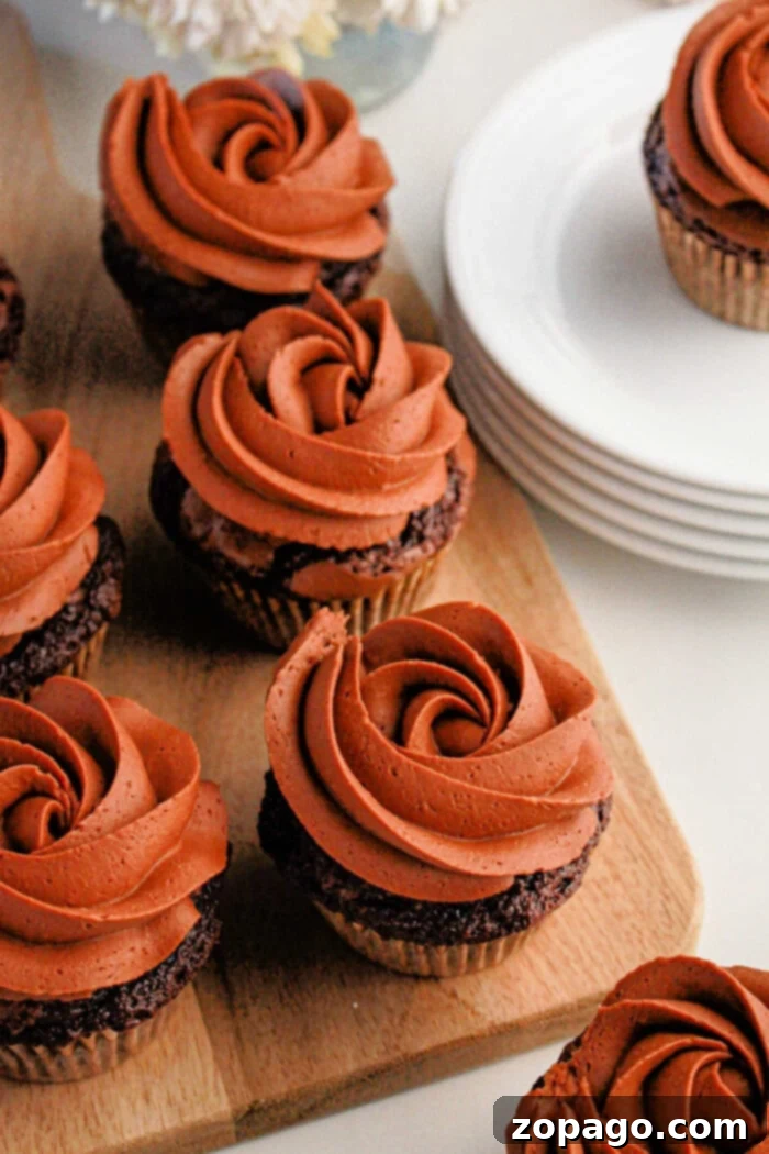 Effortless Brownie Cupcakes 6 Brownie cupcakes with swirl frosting sit elegantly on a wooden board next to stacked white plates.