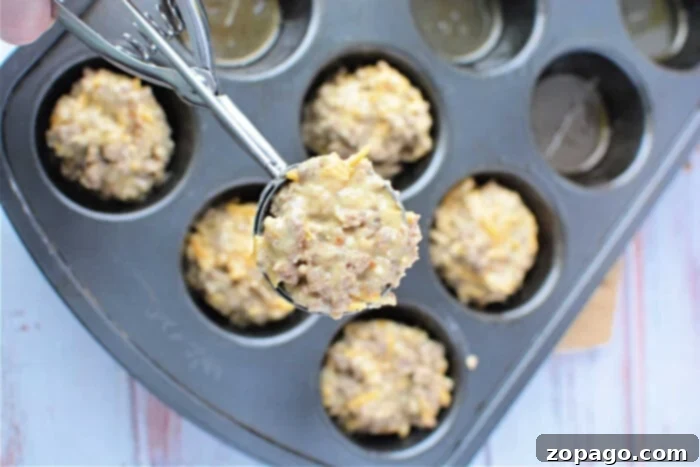 Savory Sausage Biscuits 5 A generous scoop of savory muffin batter, likely featuring Bisquick and sausage, fills a muffin pan, with other delicious muffins ready for baking on a light wooden surface. This image perfectly captures the anticipation of a hearty, homemade treat.
