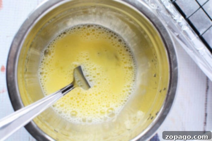 Crispy Baked Bisquick Chicken 4 Beaten eggs in a metal bowl with a fork, prepared to coat the chicken for oven-frying on a light countertop.