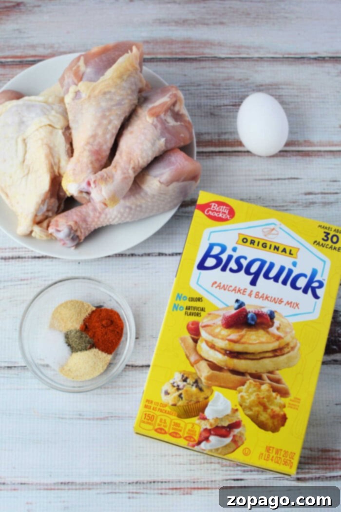 Crispy Baked Bisquick Chicken 5 Ingredients for oven-fried chicken: raw chicken drumsticks, an egg, Bisquick mix, and spices in a bowl, arranged on a rustic wooden surface.