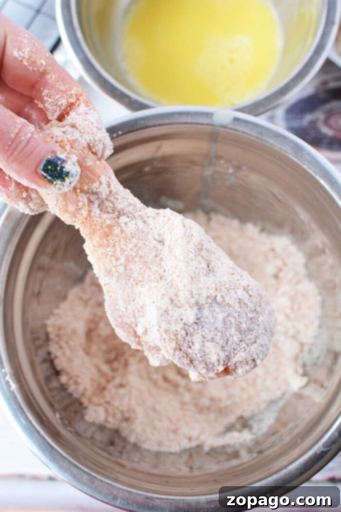 Crispy Baked Bisquick Chicken 6 A hand expertly coats a chicken drumstick in Bisquick over a mixing bowl, preparing it for delicious oven-fried chicken.