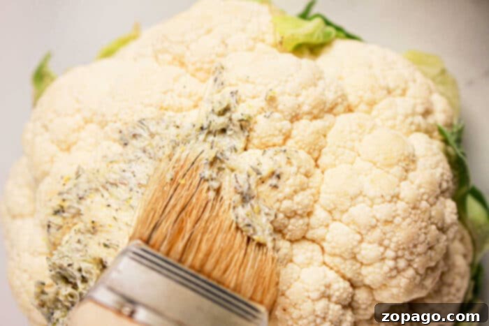 Perfect Slow Cooker Whole Cauliflower 4 Close-up of a whole cauliflower being brushed with seasoned oil or butter using a flat brush, perfect for a crock pot transformation.