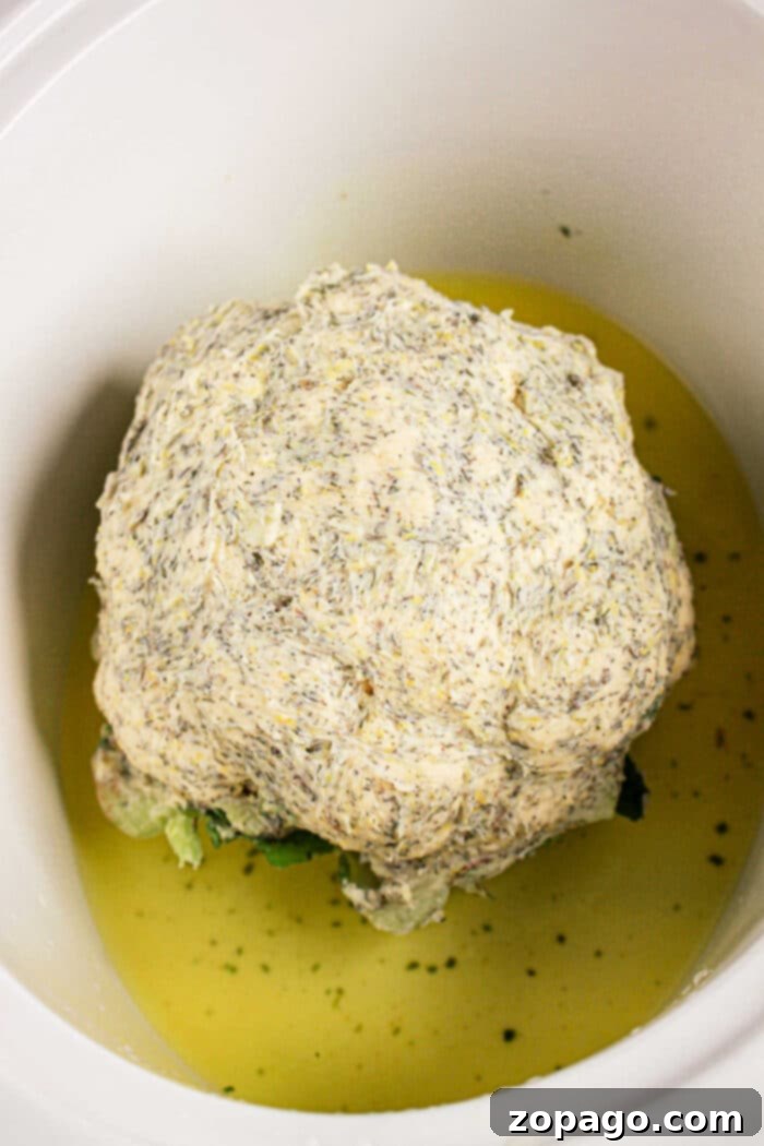 Perfect Slow Cooker Whole Cauliflower 5 A whole cauliflower head rests in a crock pot, gently coated with a seasoned sauce and partially submerged in flavorful liquid.