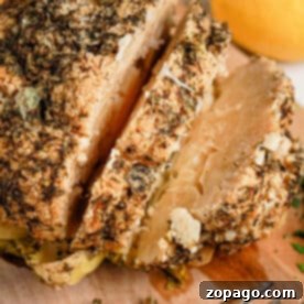 Perfect Slow Cooker Whole Cauliflower 6 A whole cauliflower head with herbs, perfectly roasted and sliced on a wooden board, sits next to a lemon and fork. This delightful cauliflower recipe is as visually appealing as it is delicious.